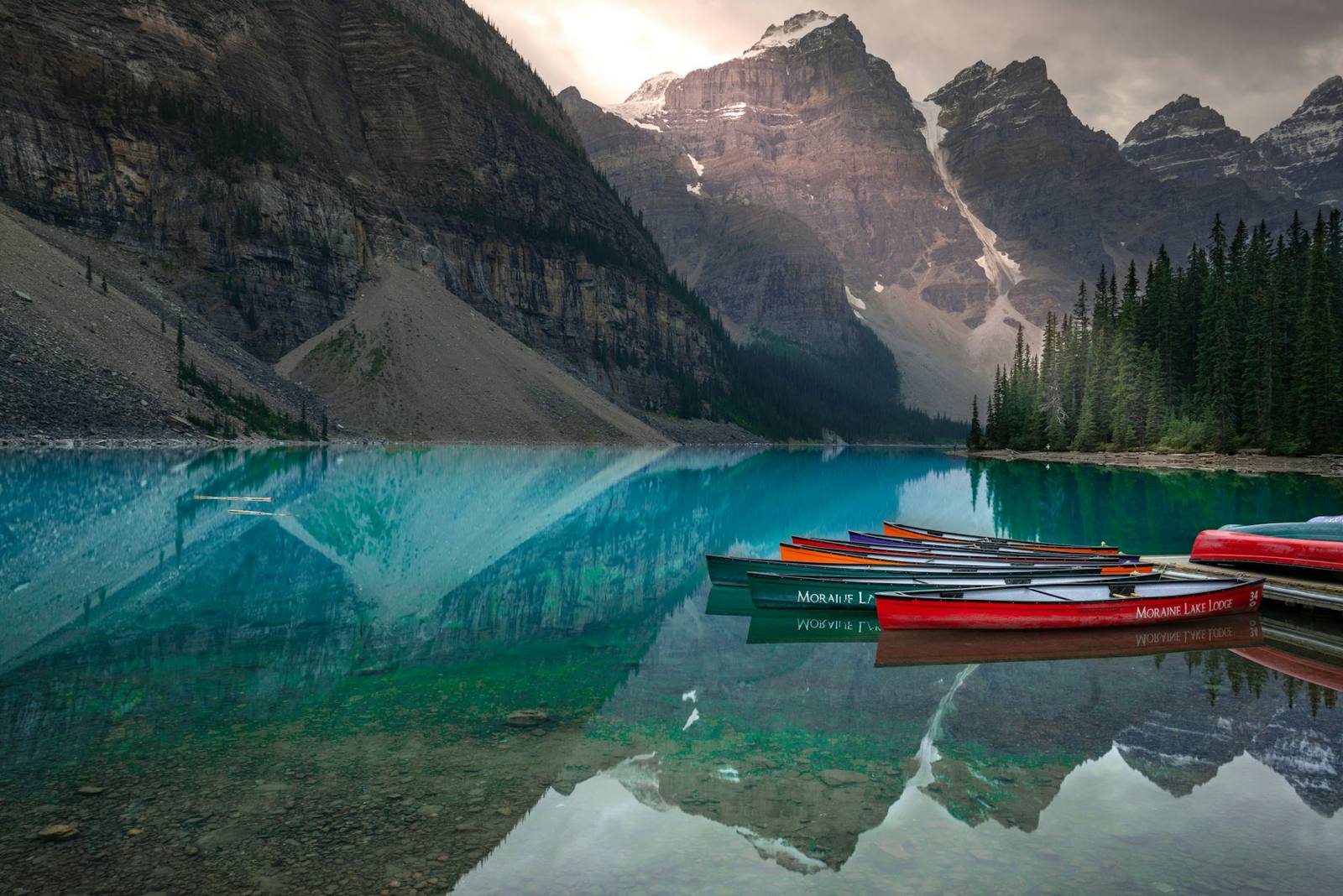 Red and yellow canoes on the turquoise water of Moraine Lake, below snowy mountains in Banff National Park